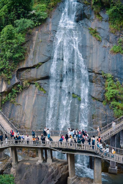 Free Tourists explore a picturesque waterfall with lush surroundings and a sturdy wooden bridge. Stock Photo