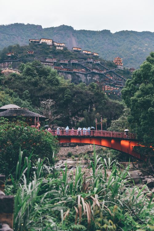 Free Charming Asian village with traditional architecture and a red bridge set in lush greenery. Stock Photo