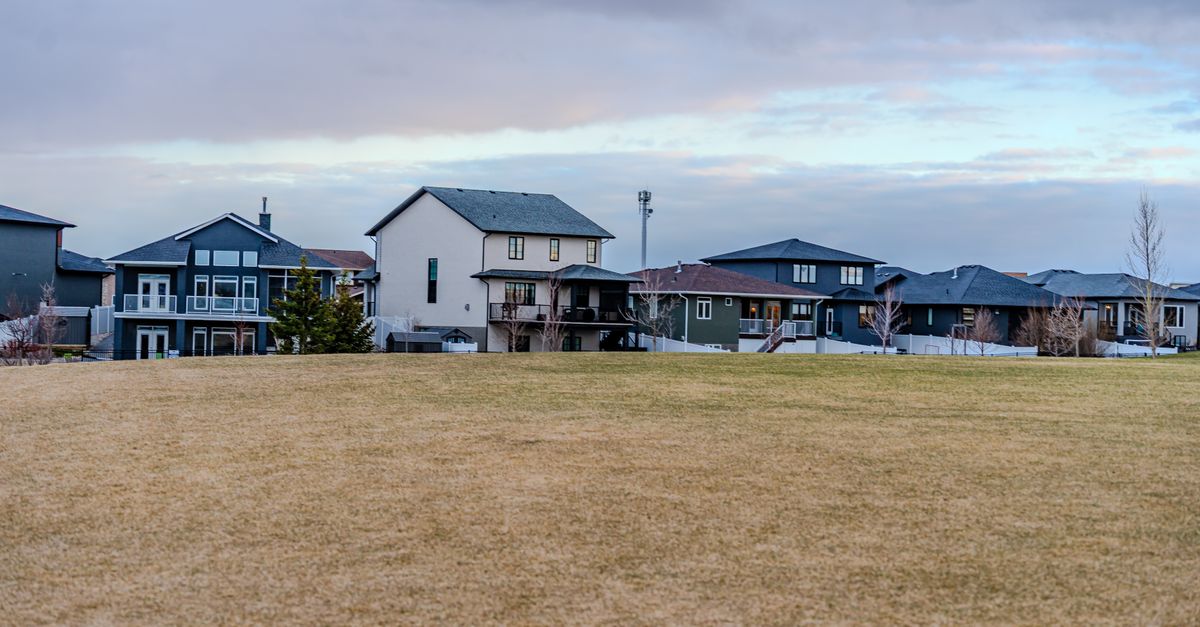 A view of suburban homes overlooking a vast open field under a partly cloudy sky.