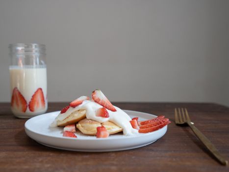 Delicious strawberry pancakes with whipped cream and a glass of milk, perfect for a hearty breakfast.