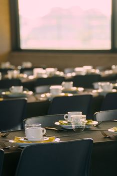 Sunlit dining room with neatly arranged tableware on dark tables, creating an elegant dining atmosphere.