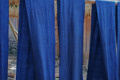 Indigo-dyed fabric dries outdoors on a rack beside bundles of straw, showcasing traditional textile methods.