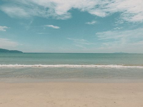 Peaceful beach scene with sandy shore, calm ocean waves, and clear blue sky.