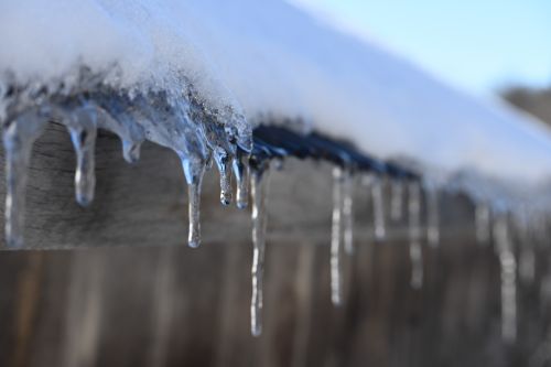 Free Detailed view of icicles hanging from a snow-covered wooden roof in winter. Stock Photo