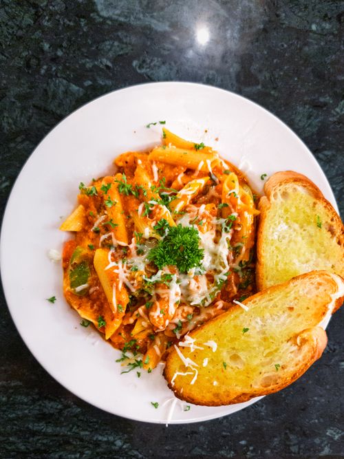Free Plate of savory penne pasta topped with cheese and parsley, served with golden garlic bread. Stock Photo
