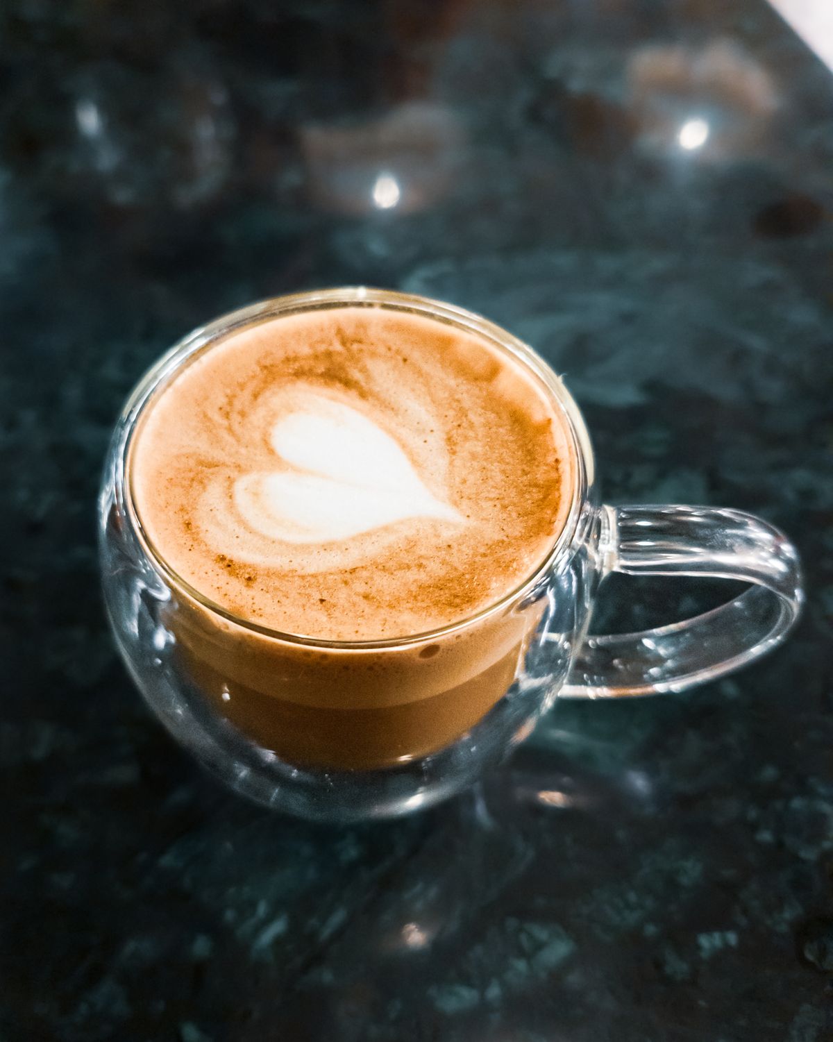 Cafe latte with a white heart of milk foam in a double-walled glass cup