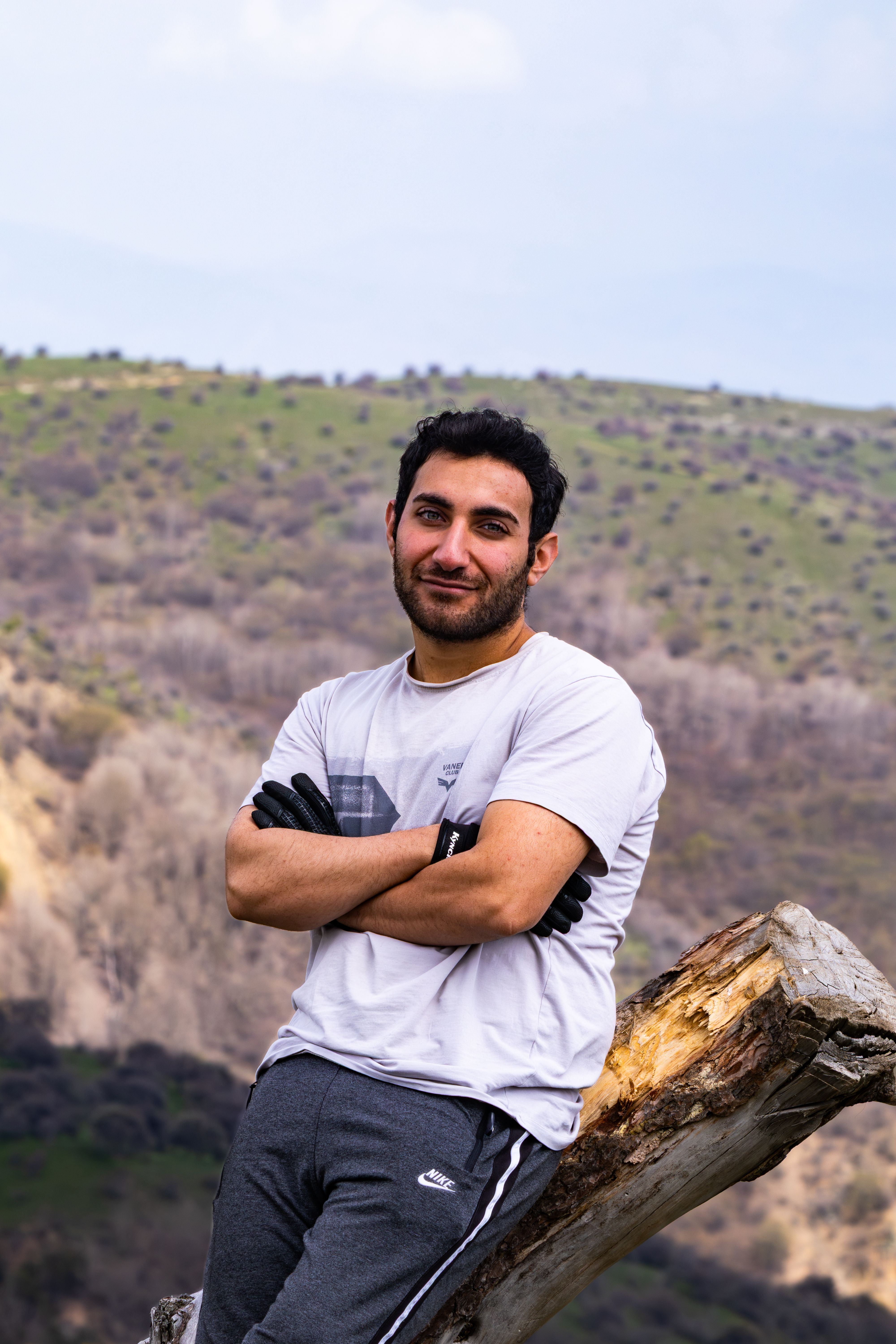 Young man posing confidently on a hill against a scenic backdrop.