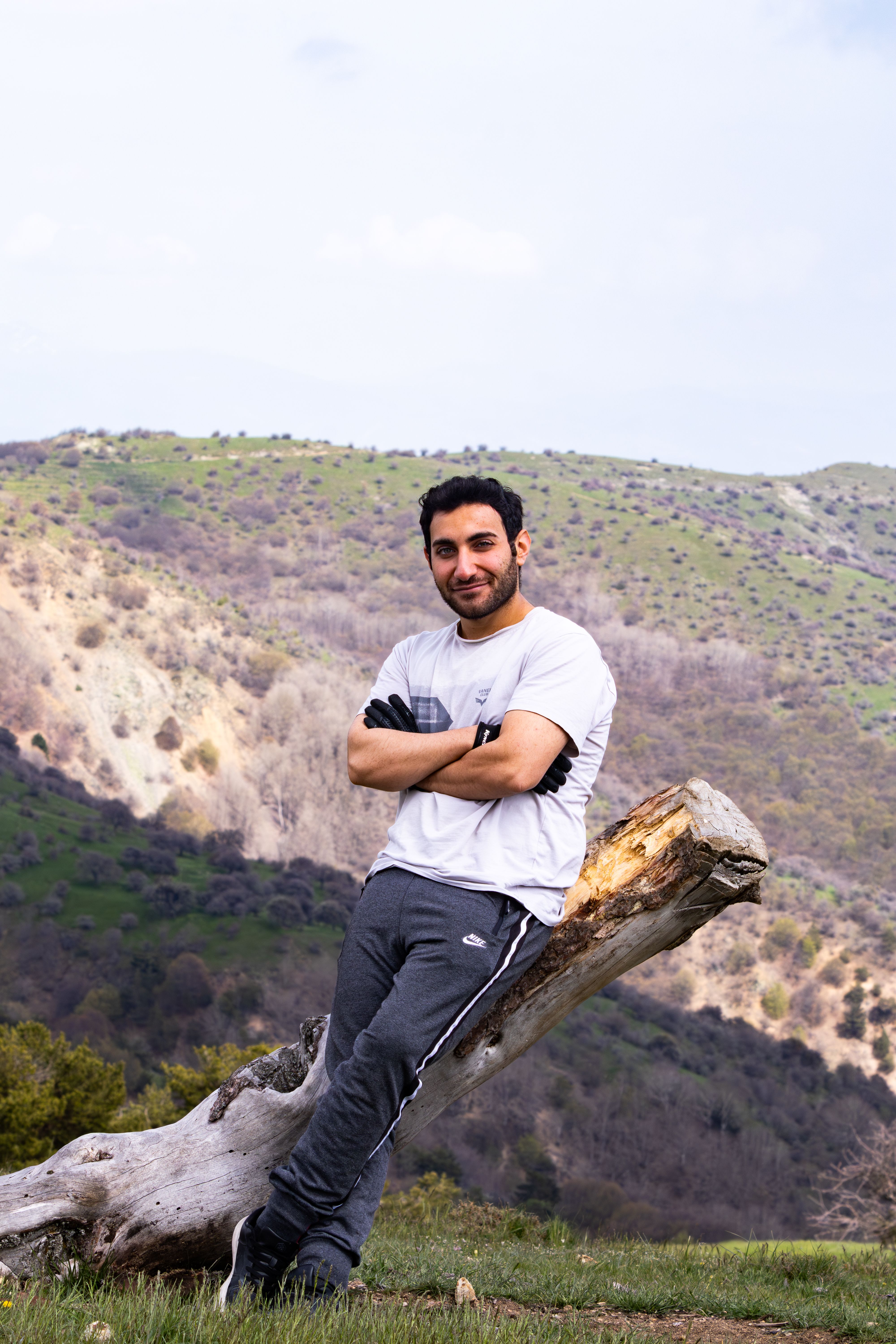 Man leaning on a log with panoramic hillside view, captured outdoors in daylight, perfect for travel or lifestyle themes.