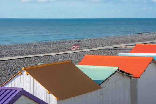 Vibrant beach huts with colorful roofs on a pebble beach by a calm sea, under a clear blue sky.