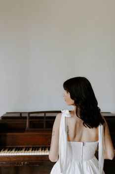A woman in a white dress stands in front of a piano, creating a serene and elegant scene.