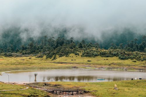 Free A peaceful misty lake surrounded by lush green hills and a tranquil forest. Stock Photo