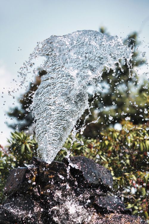 Free Captivating shot of a water fountain splash against a garden backdrop, showcasing motion and nature. Stock Photo