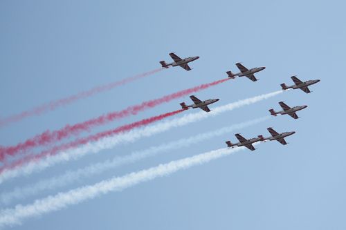 Free Five military jets perform a synchronized aerobatic display emitting red and white smoke trails against a clear blue sky. Stock Photo