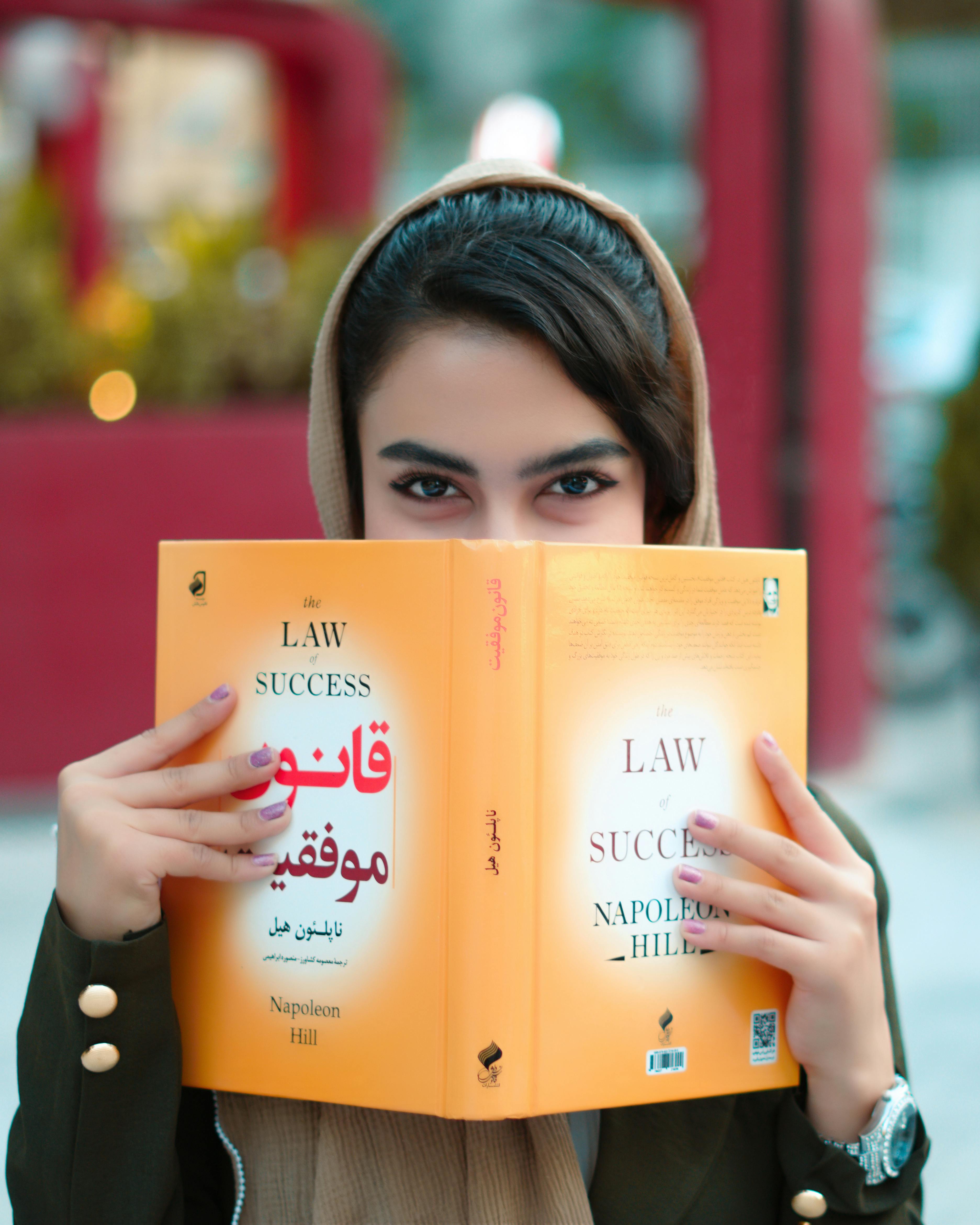Portrait of a woman reading "The Law of Success" by Napoleon Hill outdoors, focusing on the book cover.