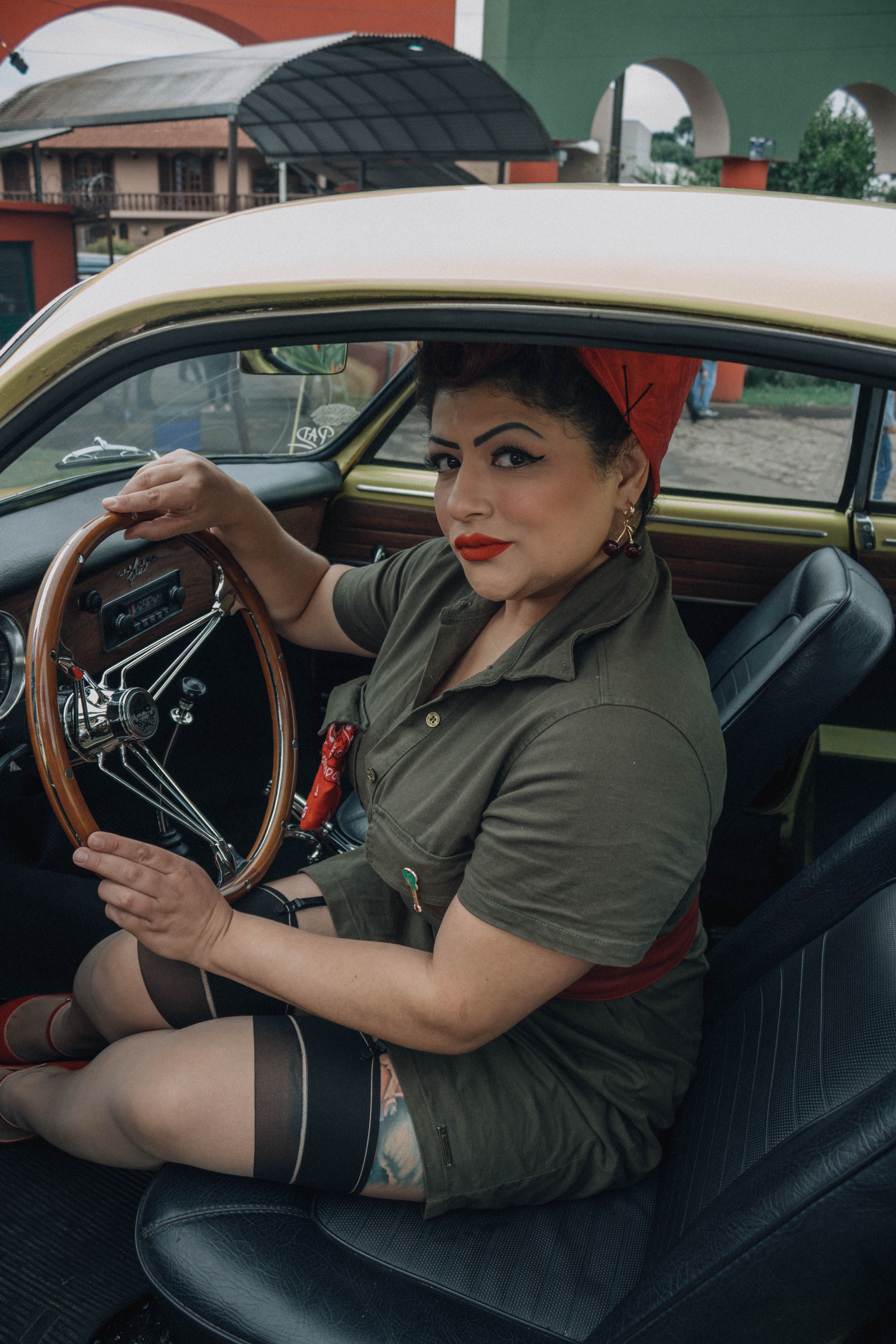 Uma mulher vestida com trajes retrô senta-se com confiança em um carro antigo, exalando estilo clássico.