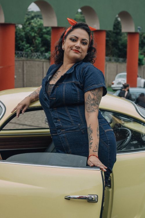 Free Confident woman in denim outfit leaning against a classic yellow car with bold tattoos and retro vibe. Stock Photo