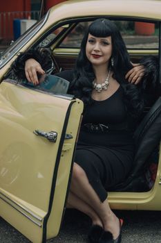Elegant woman in vintage car, exuding retro fashion with dark dress and accessories.