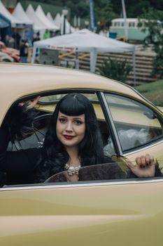 A woman with a gothic style sitting in a vintage yellow car at an outdoor event.