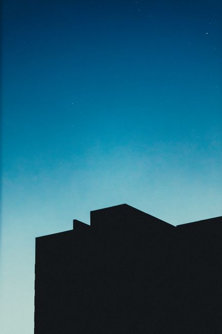 Silhouette of tall building with light halo around located against cloudless blue sky at night