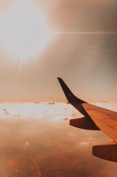 Majestic view of wing of modern airplane flying above clouds against bright sunshine on daytime