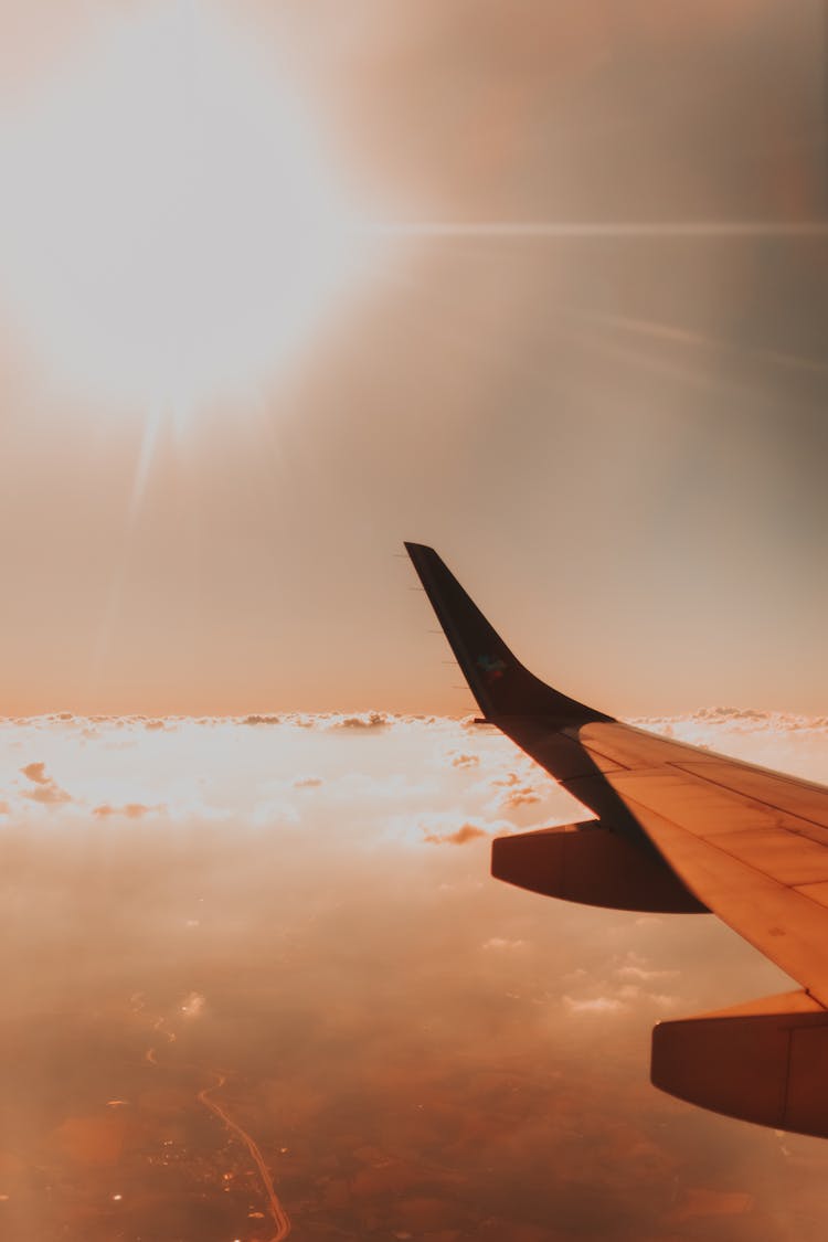 Airplane Wing Above Clouds Against Bright Sun