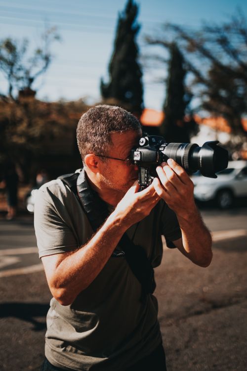 Free Male photographer in casual clothes standing on street with photo camera and taking photos on street in sunny summer day Stock Photo