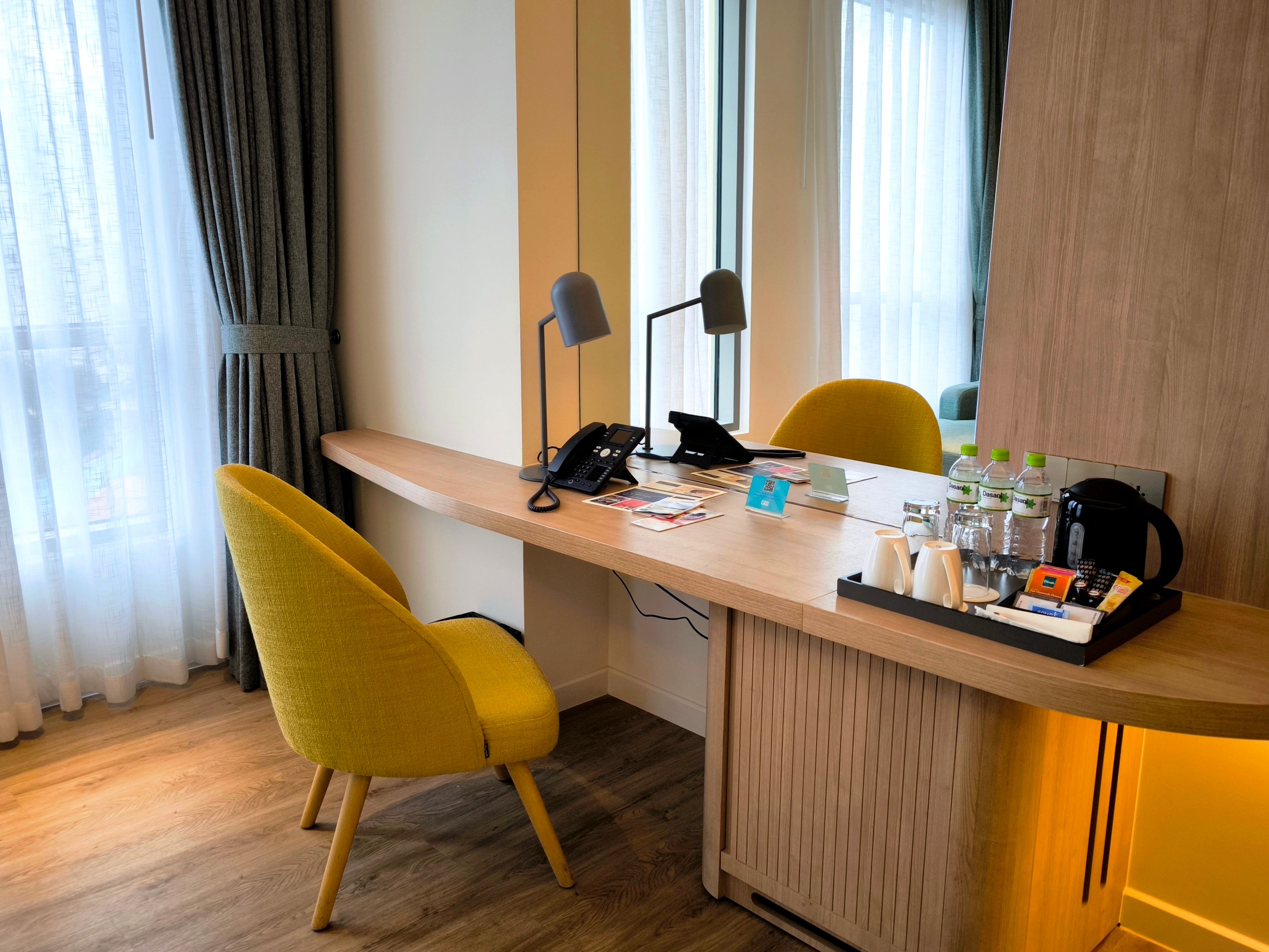 A hotel double room with blackout curtains drawn and a kettle on the desk
