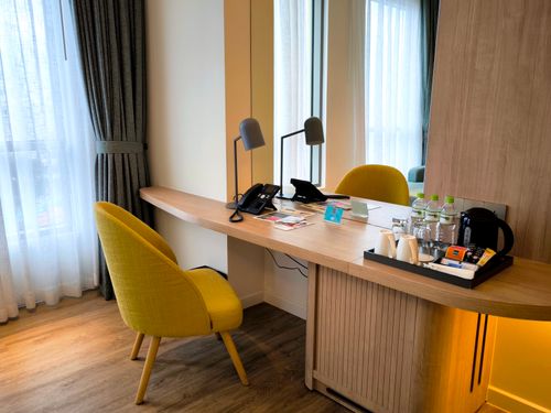 Free Stylish hotel room workspace with a wooden desk, chair, and natural light. Stock Photo