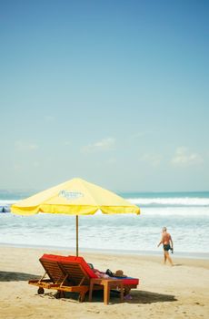 Sunny beach with yellow umbrella and lounge chairs on Bali shoreline.