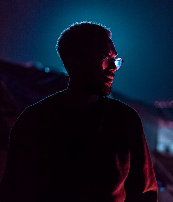 Silhouetted portrait of a man wearing glasses with vibrant blue and red backlighting.