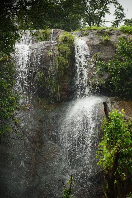 Free A serene waterfall cascades over rocky terrain surrounded by lush greenery, creating a tranquil natural landscape. Stock Photo