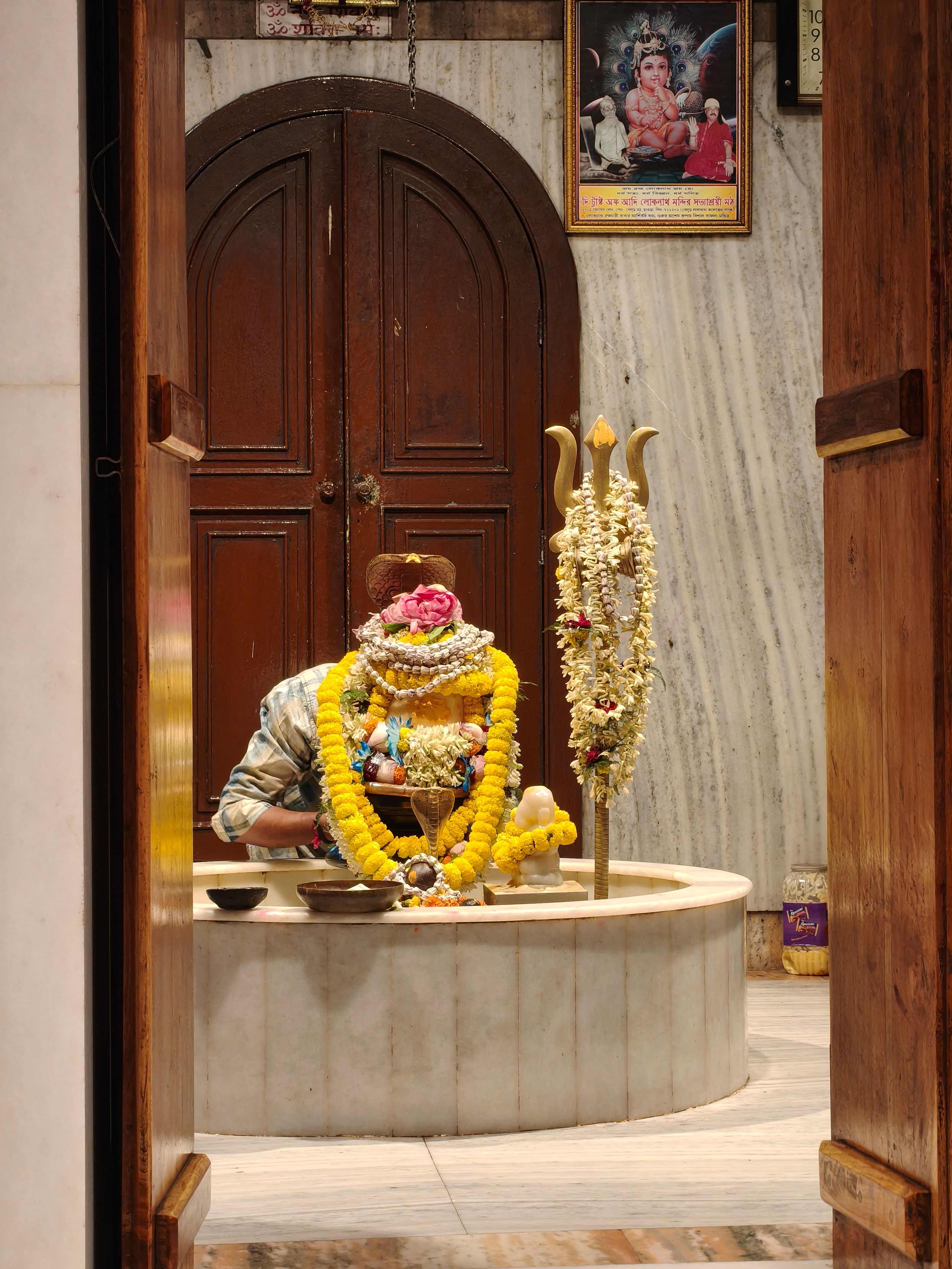 A colorful Indian shrine adorned with floral garlands, viewed through wooden doors.