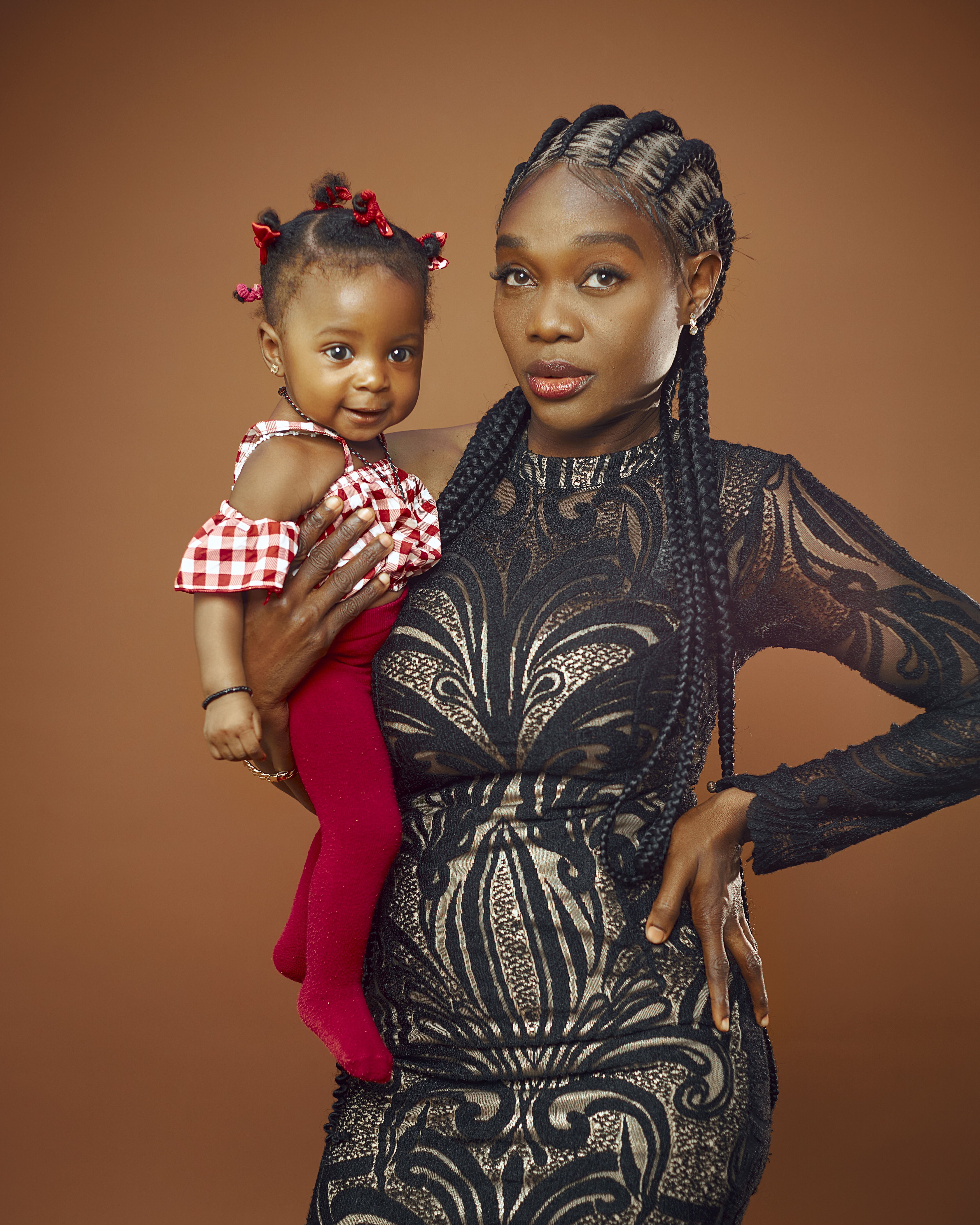 Stylish mother holding her baby daughter in a portrait against a brown backdrop, showcasing beauty and elegance.