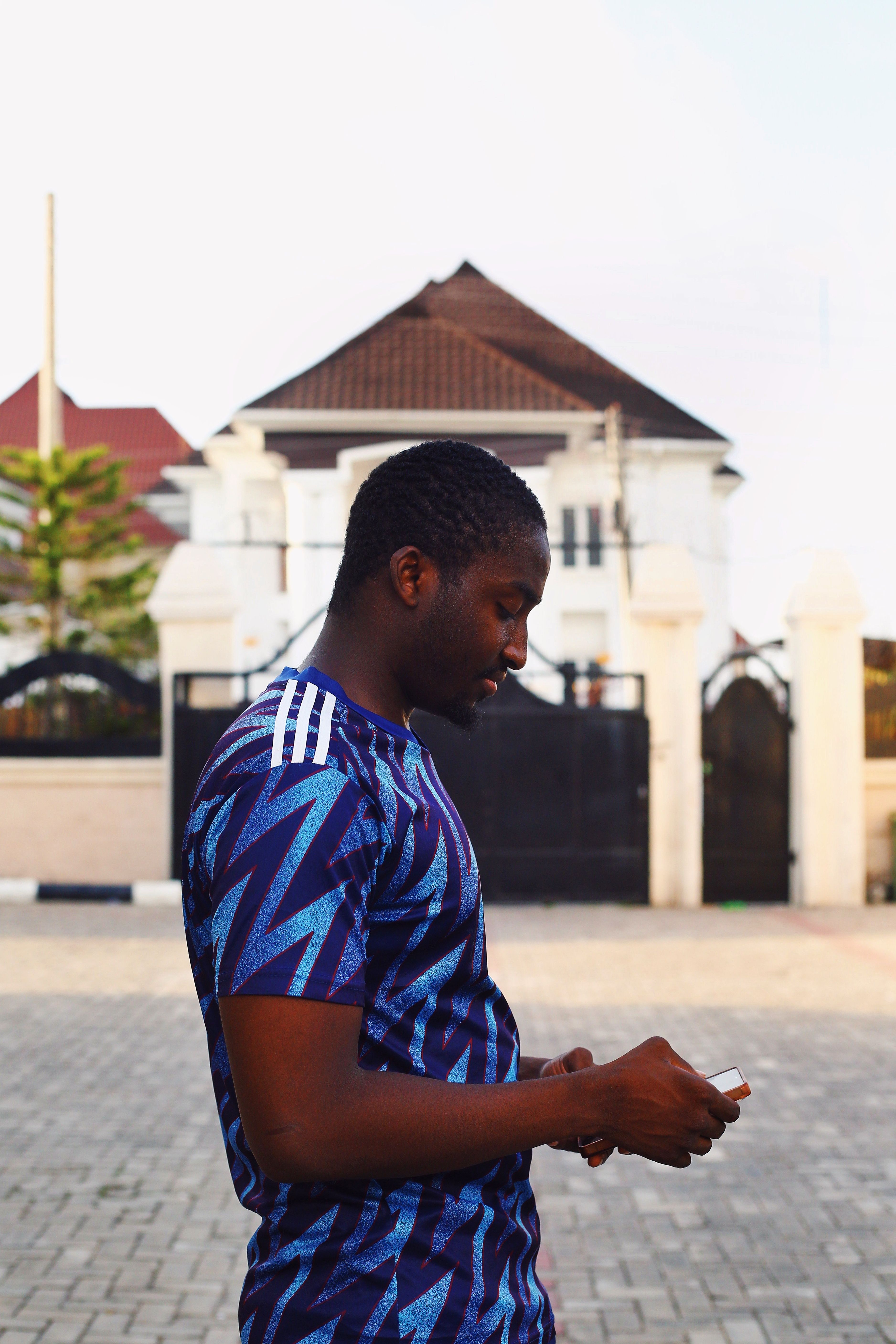 A young man in a blue patterned shirt checking his phone on a sunny day in Abuja, Nigeria.