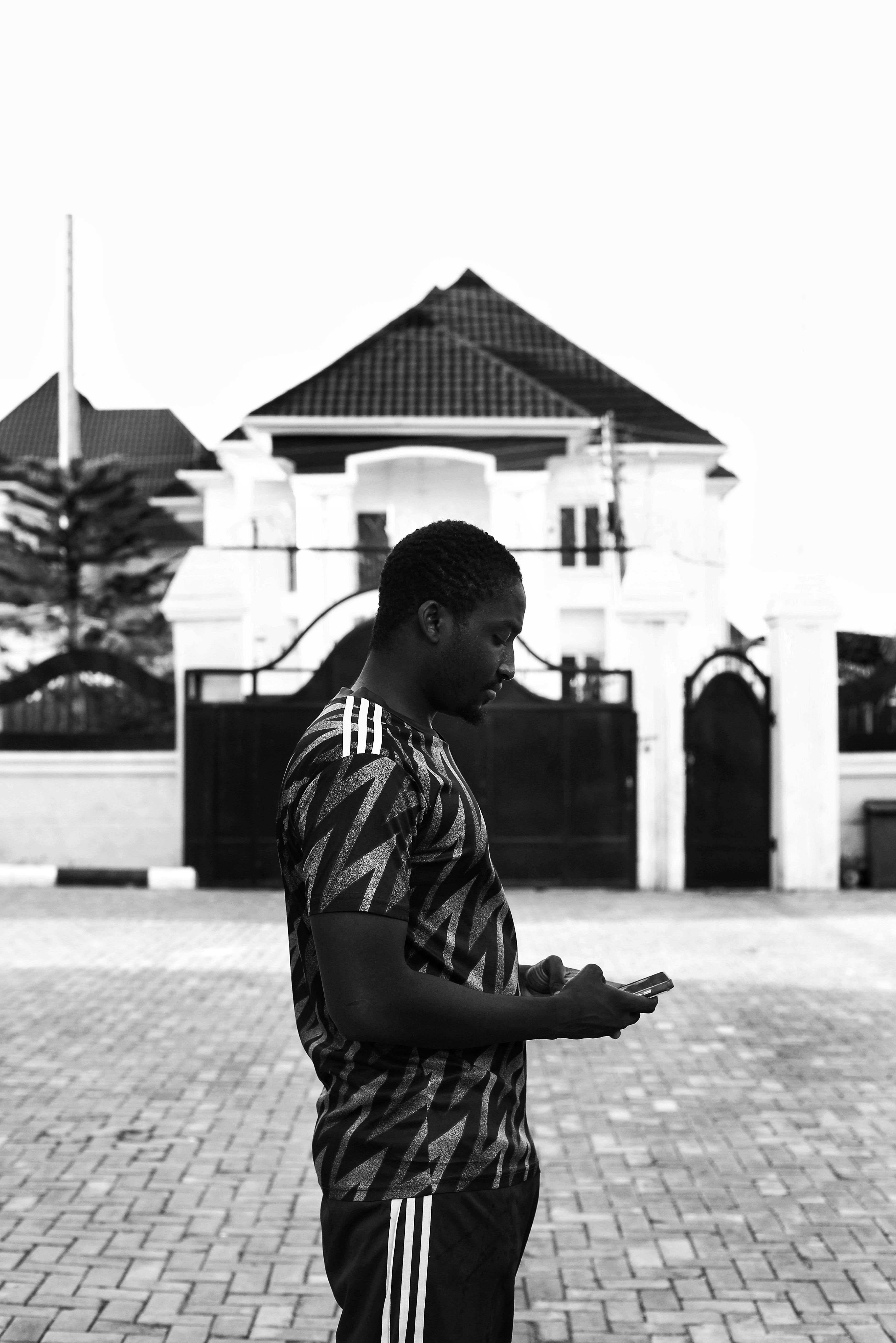 A stylish street portrait of a man using his phone, set in front of a modern house in Abuja.