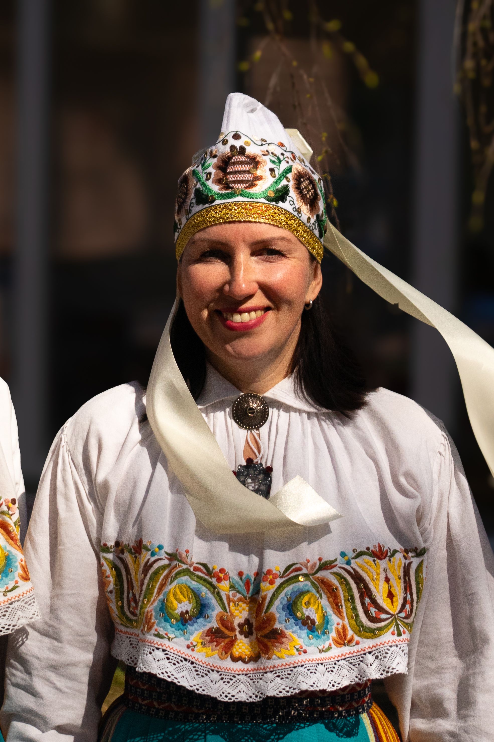 A woman wearing ornate traditional folk attire smiles outdoors, capturing a vibrant cultural moment.