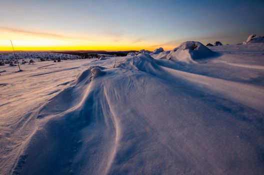 A breathtaking view of a snow-covered landscape under a vibrant sunset sky, evoking winter's calm and beauty.
