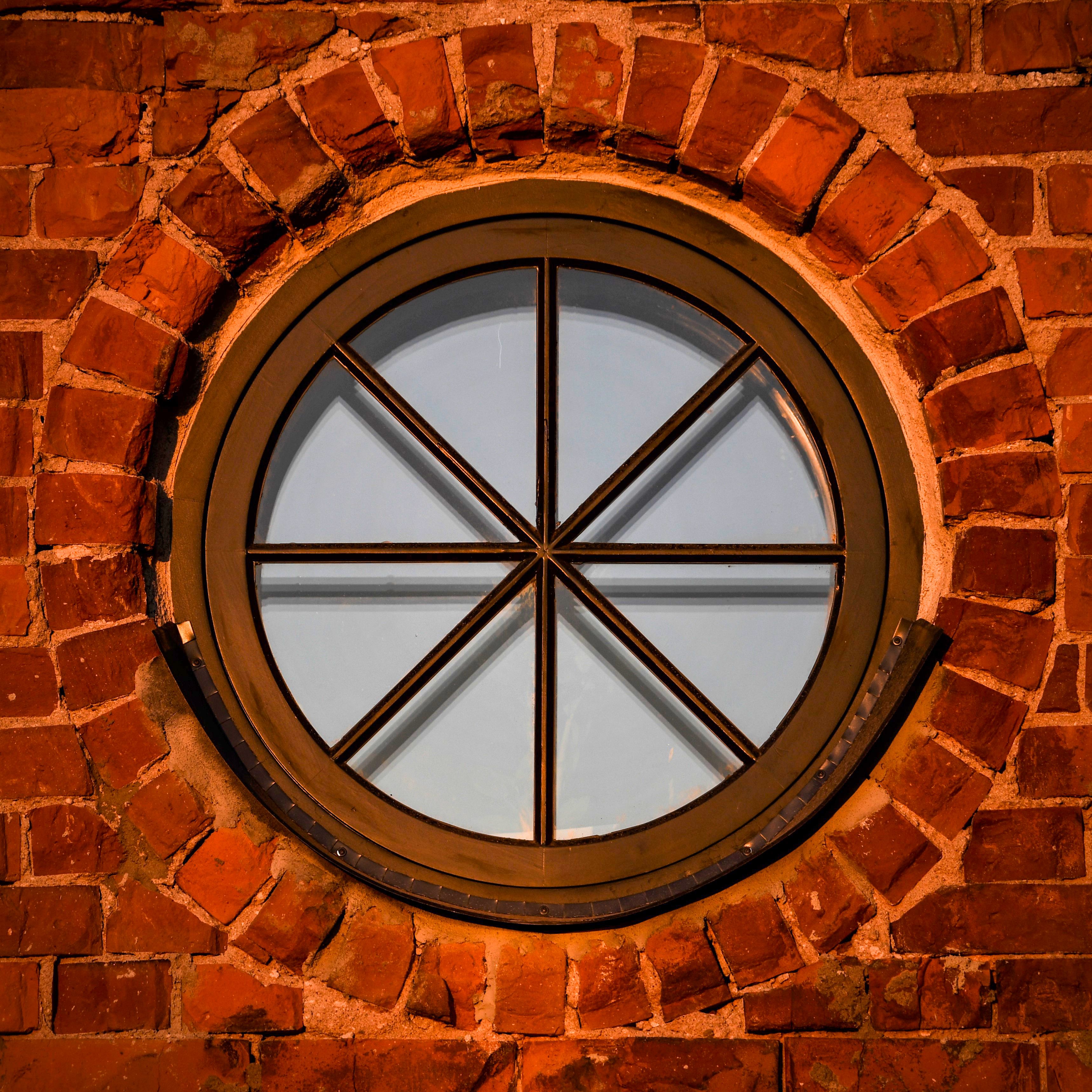 A detailed view of a vintage round window set in a red brick wall, illuminated by warm sunset light in Latvia.