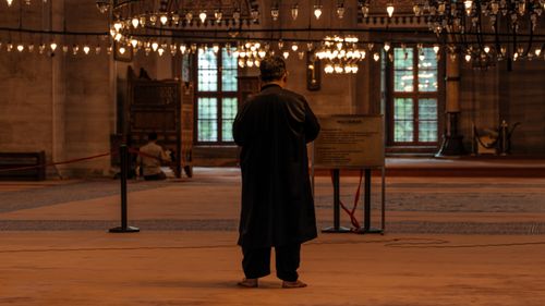 Free A man stands in contemplation inside a historic mosque with warm lighting and intricate decor. Stock Photo