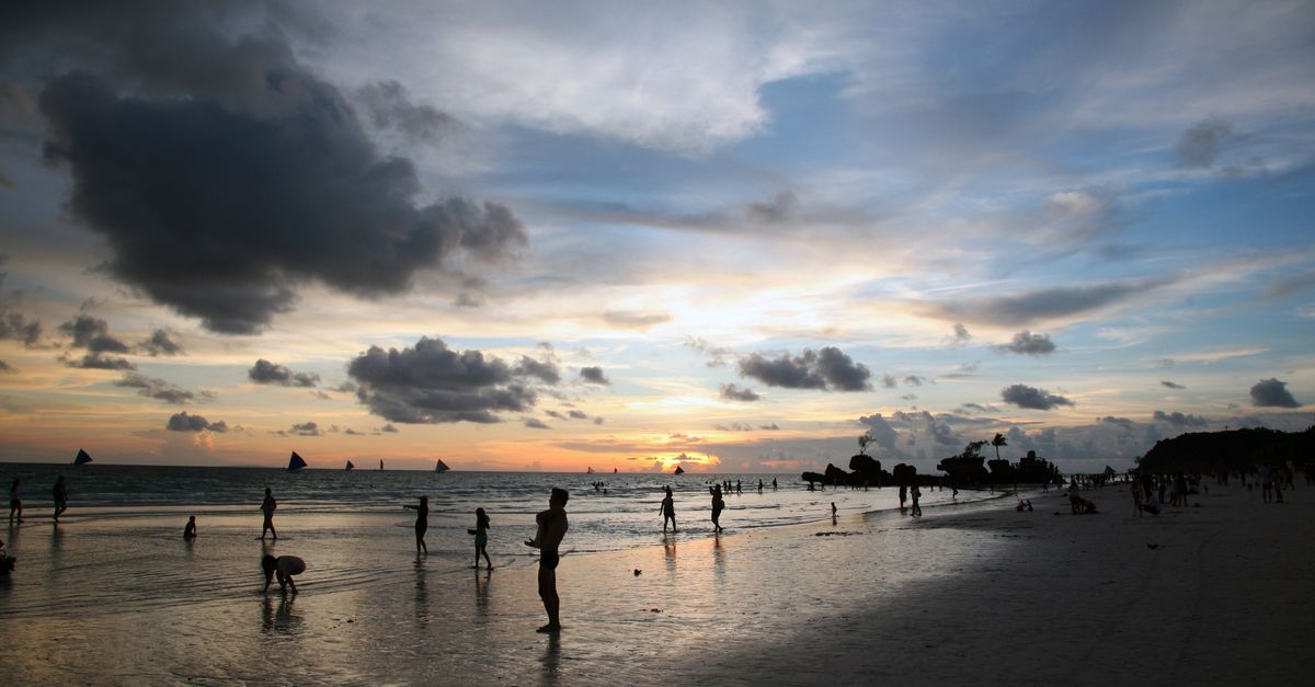 Beachgoers enjoy a stunning sunset over the ocean with silhouetted figures against a colorful sky.