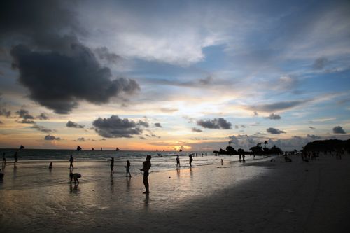 Free Beachgoers enjoy a stunning sunset over the ocean with silhouetted figures against a colorful sky. Stock Photo