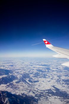 Scenic aerial view over a snowy Swiss landscape from an airplane window with clear skies.