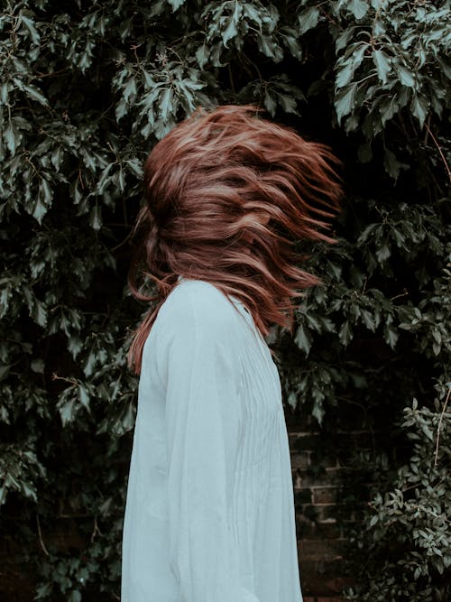 Side View Photo of Woman in White Long Sleeve Dress Standing Near Green-leafed Plant Doing Hair Flip