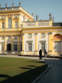 Elegant Baroque palace exterior with two adults viewing sculptures on a sunny day.