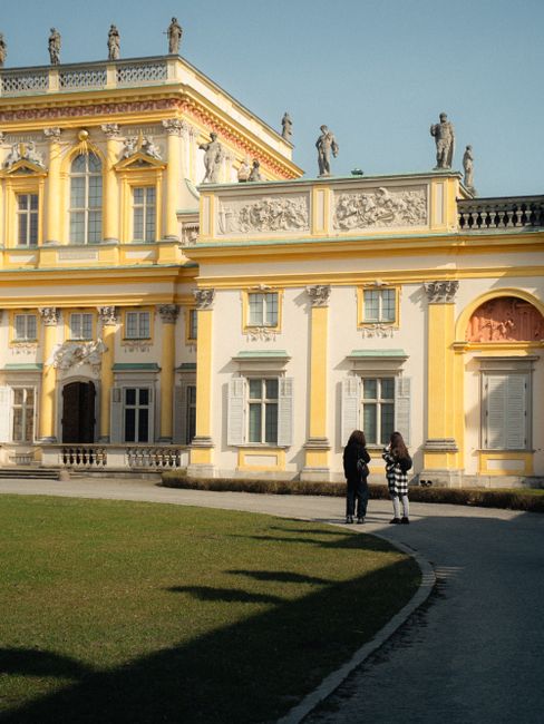 Elegant Baroque palace exterior with two adults viewing sculptures on a sunny day.