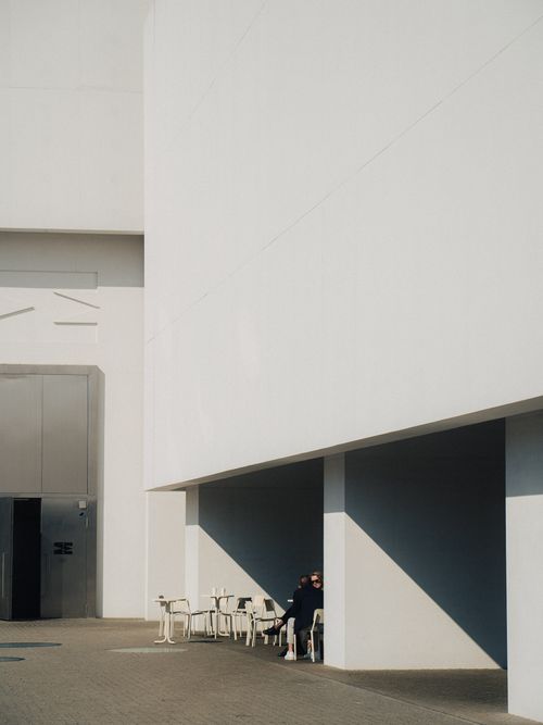 Free Minimalist urban setting with people under modern architecture, featuring strong light and shadow play. Stock Photo