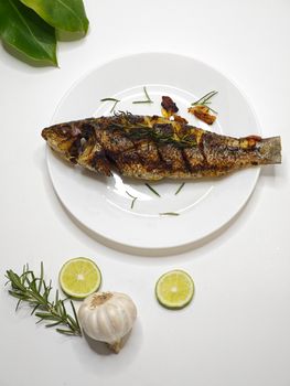 Deliciously grilled fish garnished with herbs, garlic, and lime on a white plate.