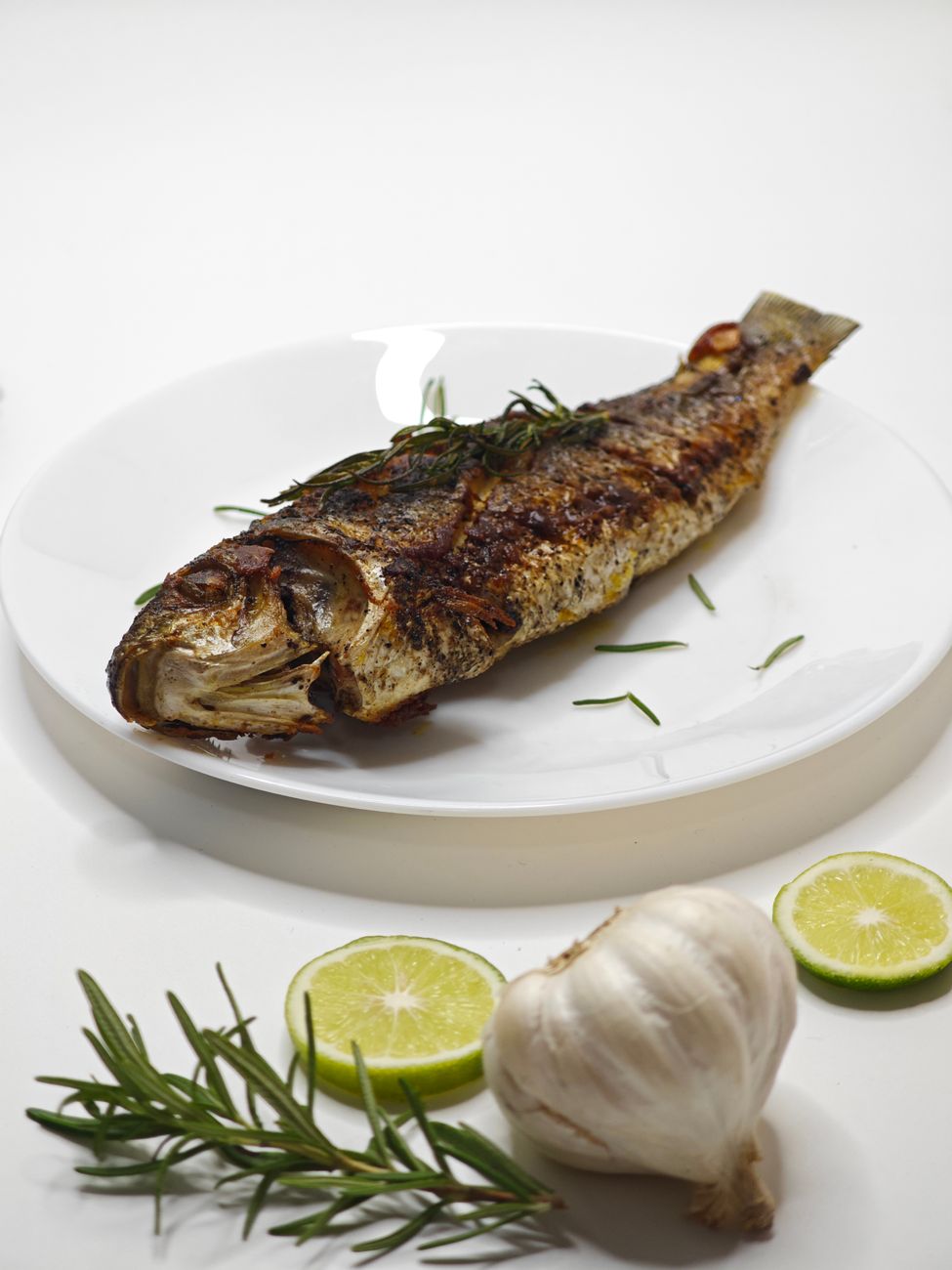 Deliciously grilled whole fish paired with rosemary, lime, and garlic on a white plate.