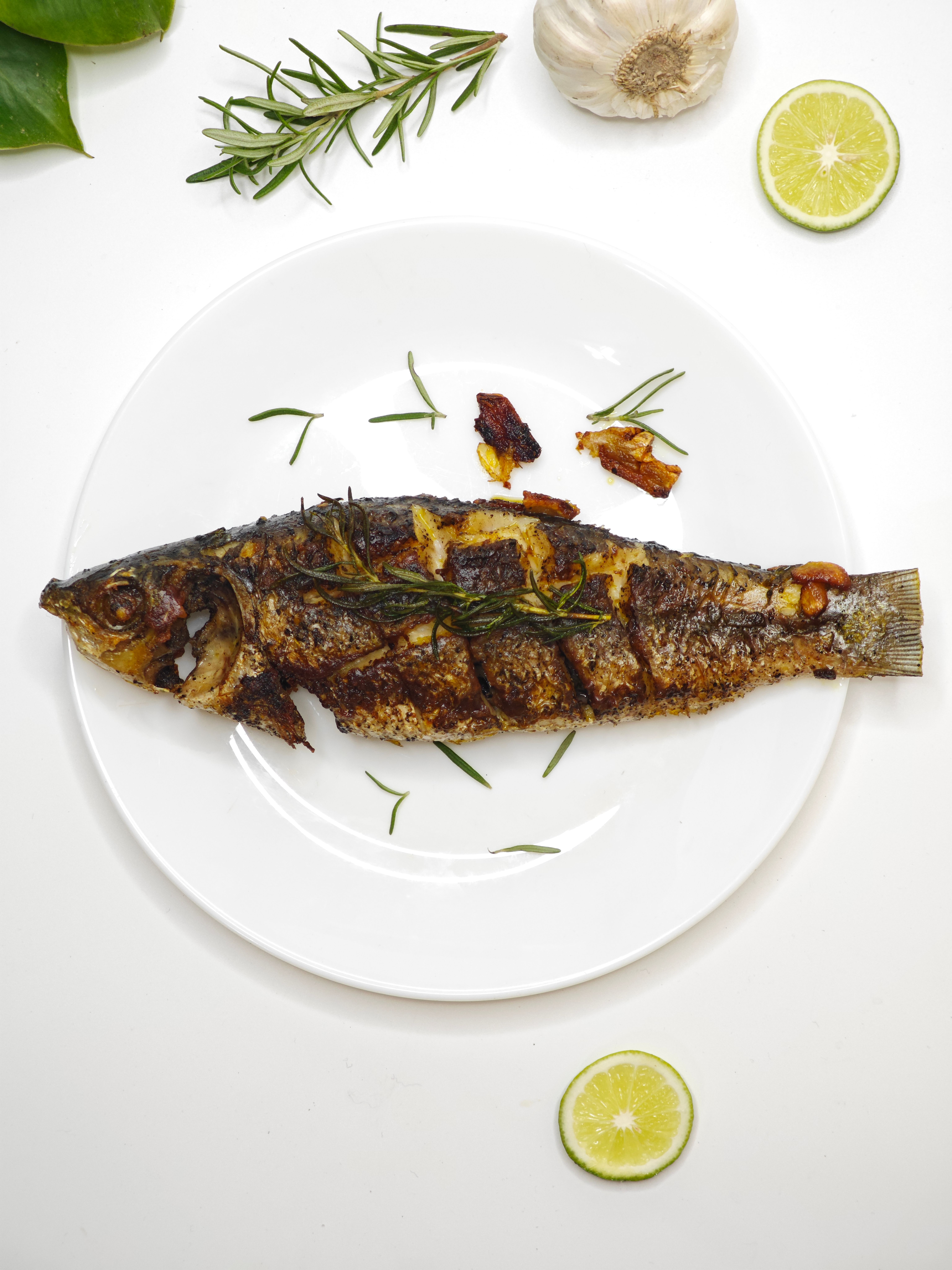 Delicious whole grilled fish garnished with rosemary, garlic, and lime for a tasty presentation.