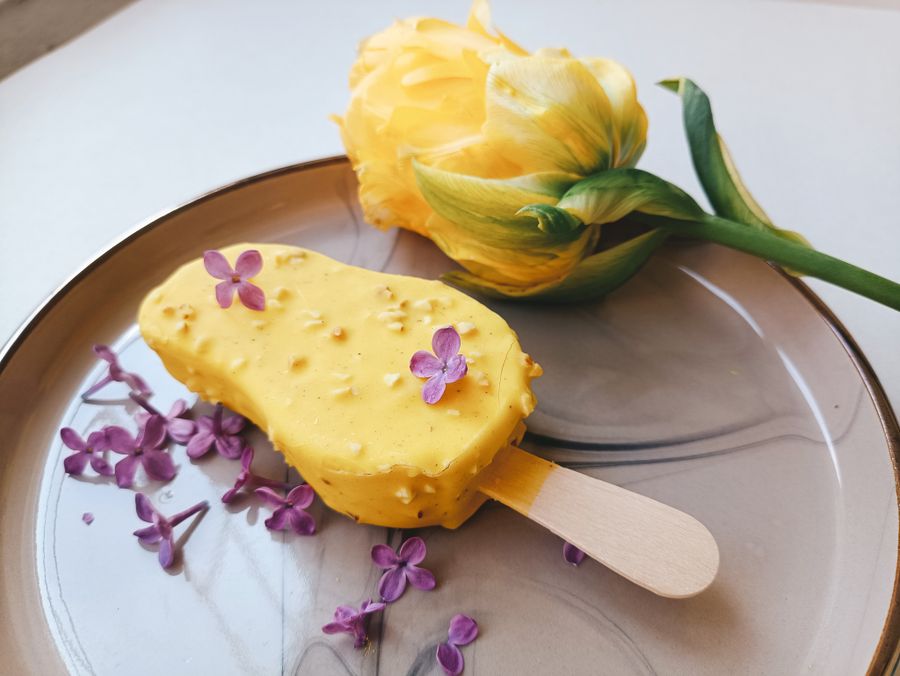 Saffron-yellow kesar kulfi stick on a plate with flowers
